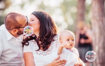 A tender family moment captured with a couple kissing and a baby holding bubbles outdoors.
