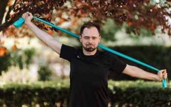 Adult man in black shirt exercises with a resistance band outside.