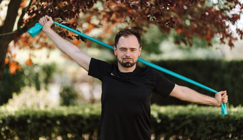 Adult man in black shirt exercises with a resistance band outside.